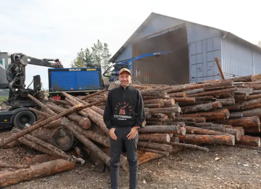 Mann står foran en haug med tømmerstokker