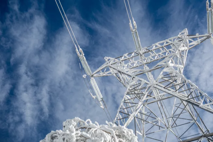 En telekommunikasjons-mast med frost og snø fra froskeperspektiv, med en blå og lett skyet himmel i bakgrunnen.