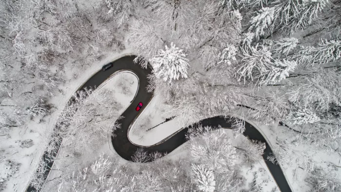 Luftfoto av en snødekket skog med en snirklete svart vei med en rød bil.