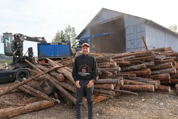 Mann står foran en haug med tømmerstokker